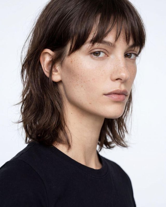 AI-generated portrait of a woman with visible skin texture and freckles, front lighting against a plain background
