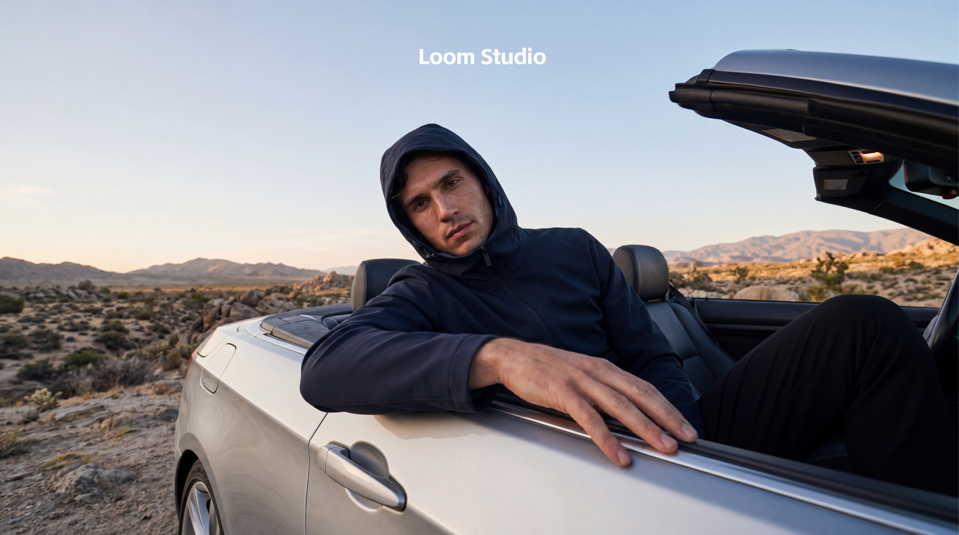 Mojave Mirage: Precision Tailoring and Cinematic Desert Light High-end AI generated fashion photography of a male model in a navy hooded technical jacket, demonstrating realistic fabric rendering in a luxury convertible car set against a detailed Mojave Desert background at sunset.