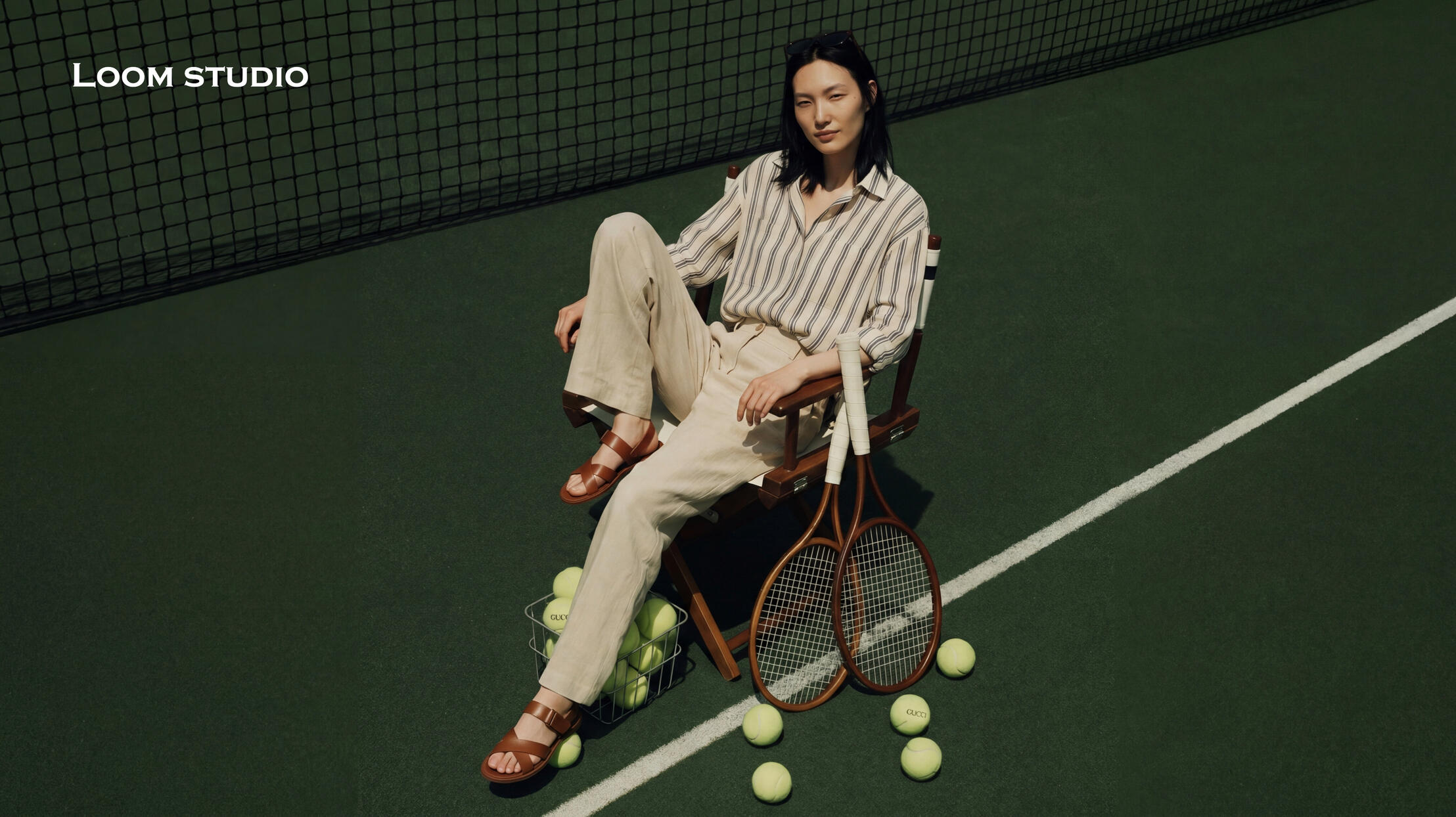 Courtside Leisure: The Linen and Stripe Edit AI-generated fashion editorial of a model on a green tennis court wearing a striped linen shirt, beige trousers, and leather sandals. High-end lifestyle imagery by Loom Studio showcasing realistic fabric textures and lighting